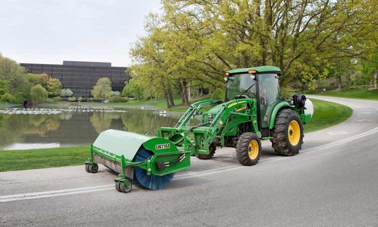 John Deere loader with broom attachment sweeping debris from a road