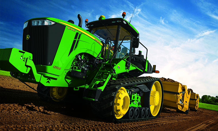 Tracked tractor pulling a John Deere scraper across dirt with blue sky ...