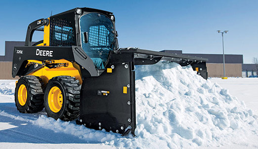 Skid Steer with Snow Pusher attachment clearing snow in a parking lot