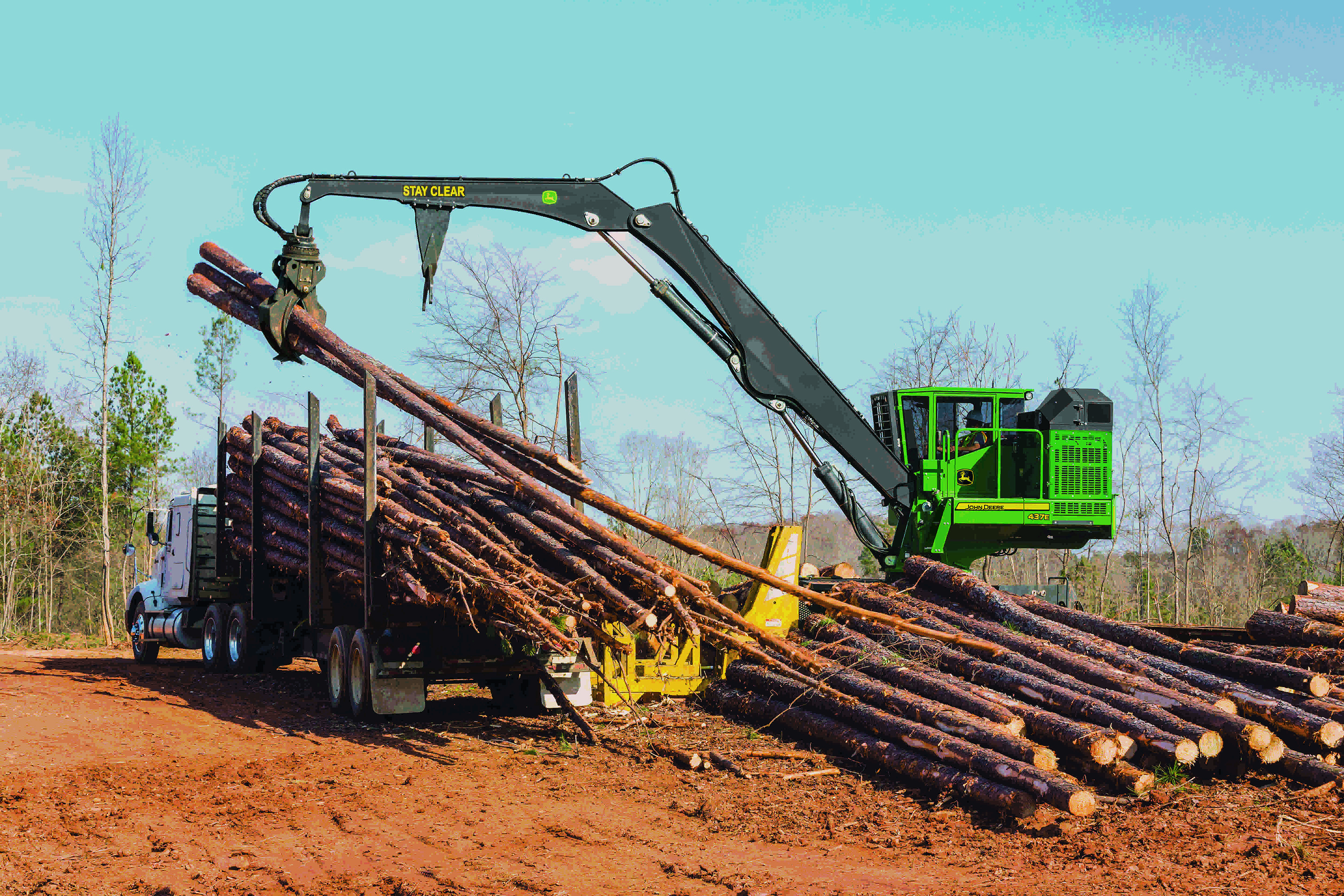 The John Deere 437E knuckleboom loader piling logs at a jobsite.